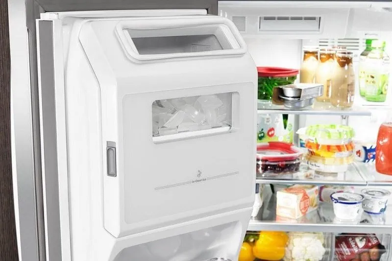 An open refrigerator door reveals a built-in ice maker with ice cubes inside, while the shelves in the fridge hold drinks, eggs, condiments, and various food containers.
